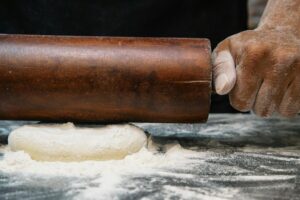 Close-up of a chef rolling dough with a wooden pin, capturing the art of baking.